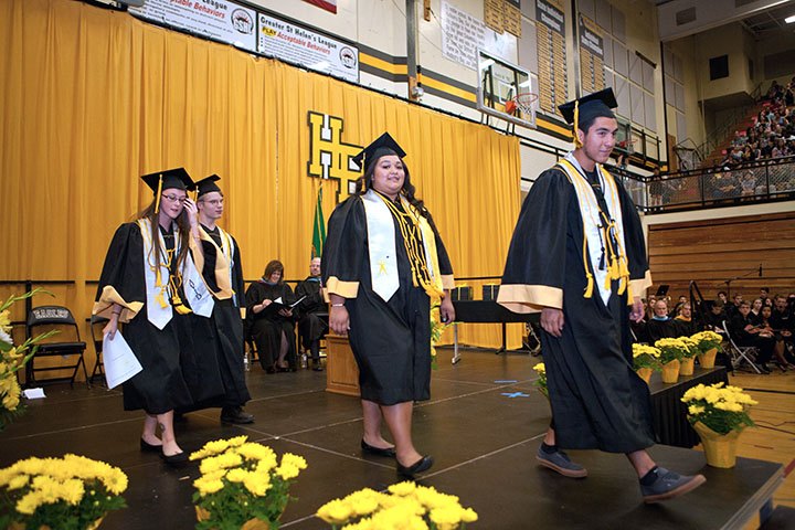 Graduates in their regalia cross the stage at commencement